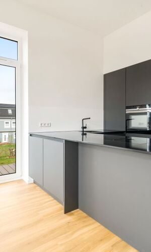 Moderne Küche mit schwarzer Kücheninsel, integriertem Backofen und großem Fenster mit Blick auf Nachbargebäude