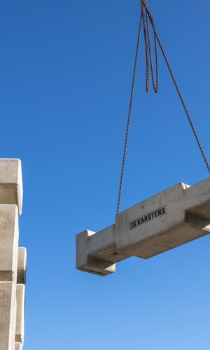 Betonfertigteil mit der Aufschrift 'HK Karstens' wird von einem Kran gehoben, weitere Betonfertigteile im Hintergrund