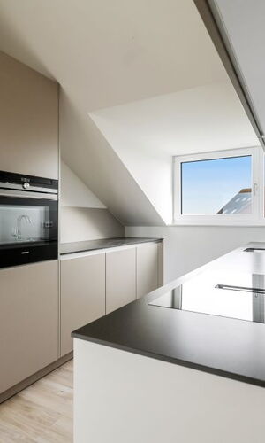 Moderne Küche mit grauen Einbauschränken, Backofen, Kochfeld und Fenster unter Dachschräge
